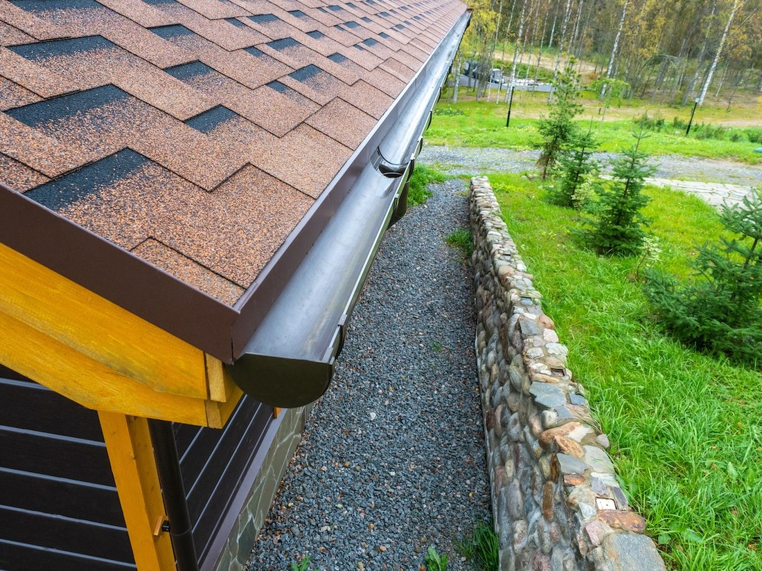 A gutter running along the edge of a shingled roof